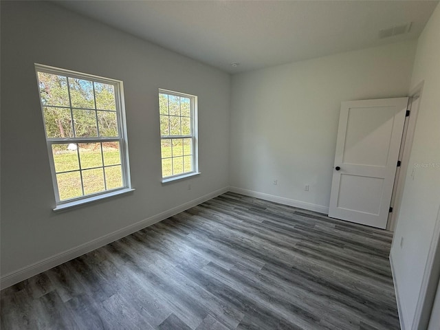 empty room with visible vents, dark wood-type flooring, and baseboards