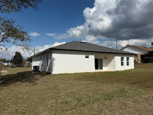 back of property with a yard, central AC unit, roof with shingles, and stucco siding