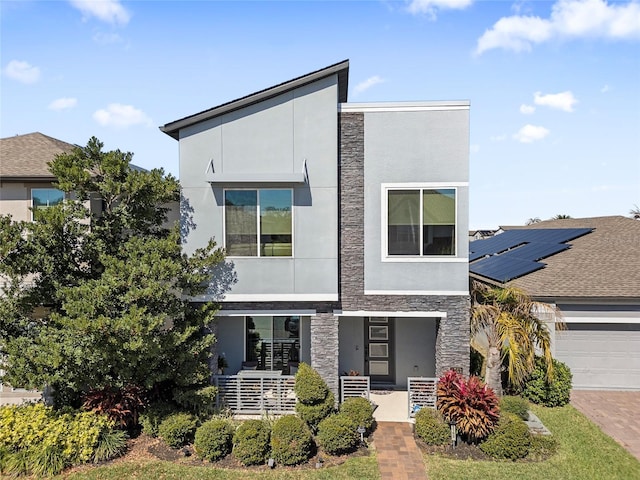 contemporary home with a garage, stone siding, decorative driveway, a porch, and stucco siding