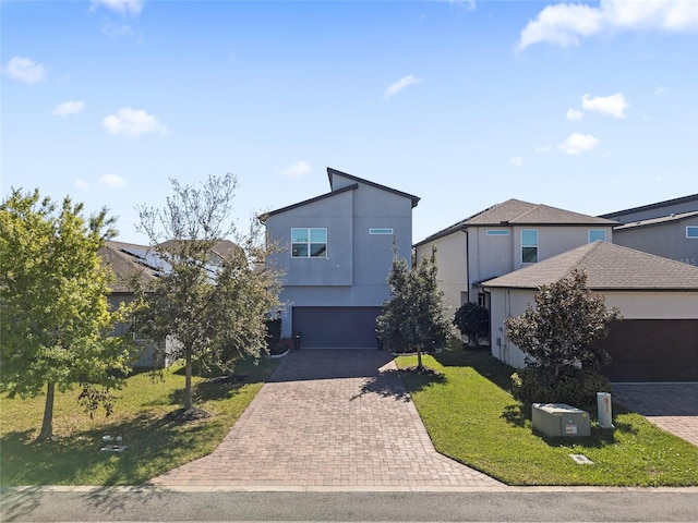 view of front of property with decorative driveway, stucco siding, an attached garage, a front yard, and central AC