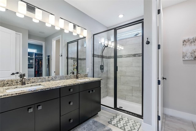 bathroom with a stall shower, a spacious closet, baseboards, and a sink