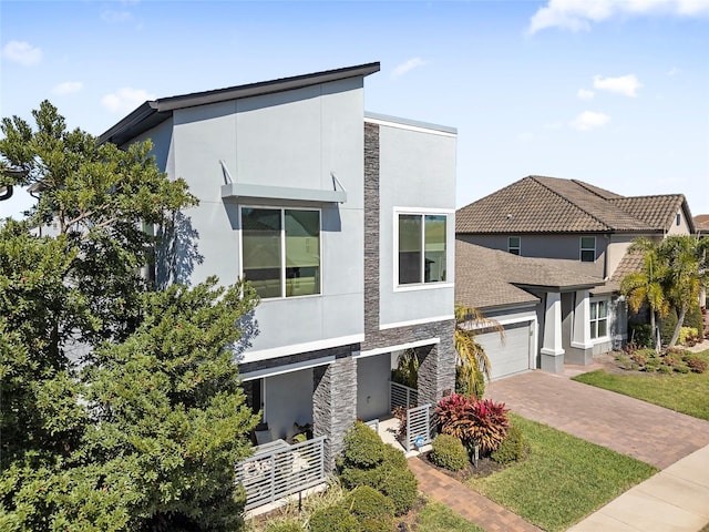 contemporary home with a garage, stone siding, decorative driveway, and stucco siding