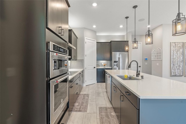 kitchen featuring stainless steel appliances, a sink, light countertops, an island with sink, and decorative light fixtures