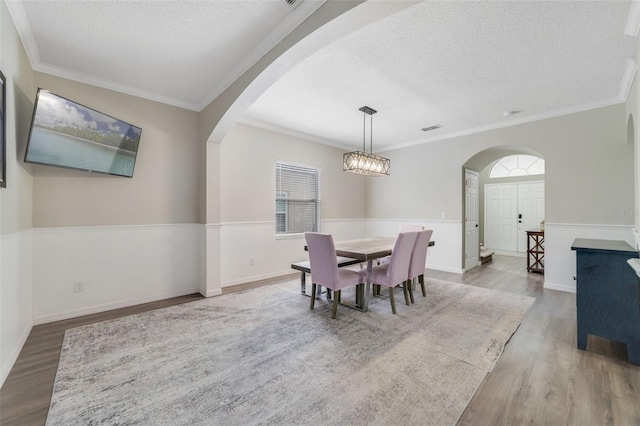 dining area featuring arched walkways, ornamental molding, a textured ceiling, and wood finished floors