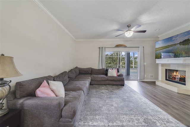 living room featuring a warm lit fireplace, ceiling fan, a textured ceiling, wood finished floors, and crown molding