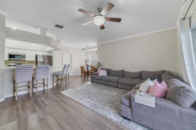 living area with visible vents, ceiling fan, ornamental molding, a textured ceiling, and light wood-style floors