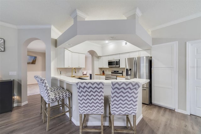 kitchen featuring white cabinets, appliances with stainless steel finishes, a breakfast bar, a peninsula, and light countertops