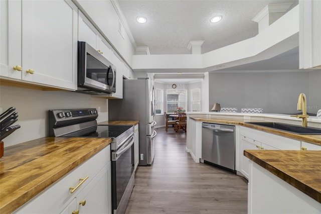 kitchen featuring ornamental molding, stainless steel appliances, white cabinetry, wooden counters, and a sink