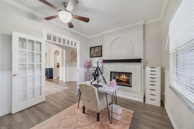 sitting room with ornamental molding, arched walkways, wood finished floors, and a tile fireplace