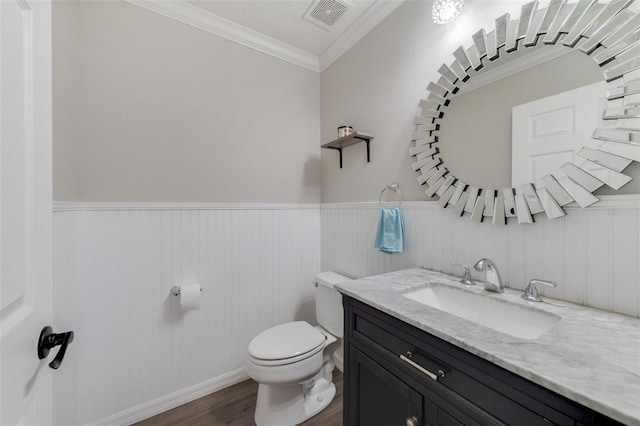 half bath with toilet, wood finished floors, vanity, visible vents, and crown molding