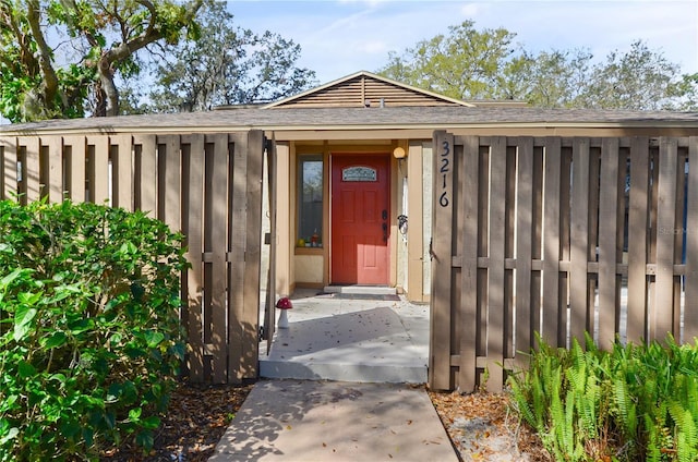 entrance to property featuring a shingled roof and fence