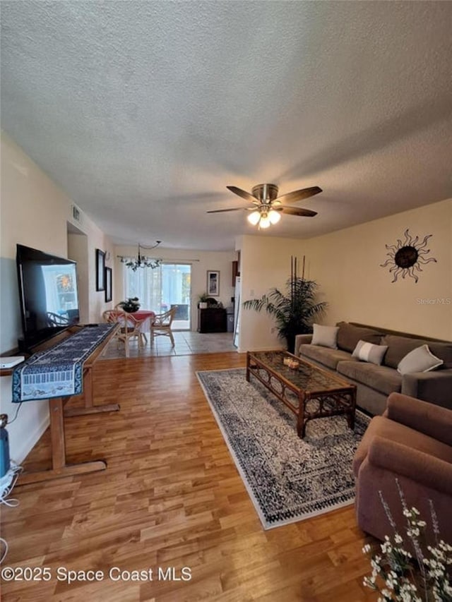 living room with ceiling fan with notable chandelier, light hardwood / wood-style floors, and a textured ceiling