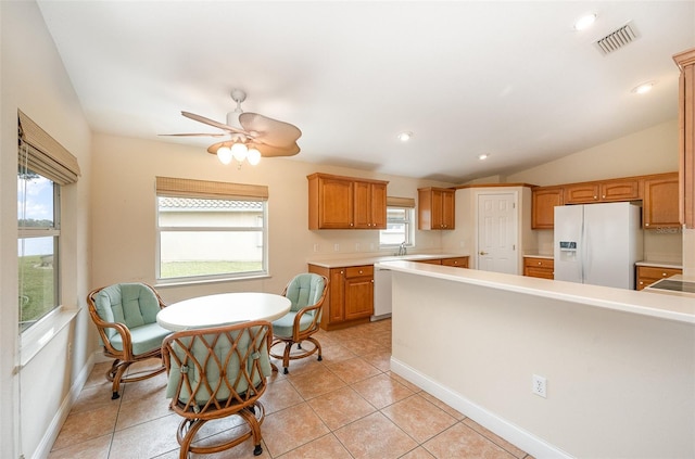 kitchen featuring vaulted ceiling, sink, white fridge with ice dispenser, light tile patterned floors, and ceiling fan