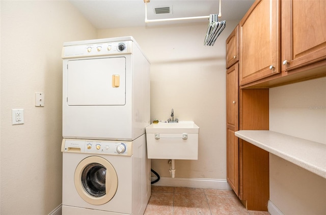 laundry area with cabinets, light tile patterned flooring, and stacked washer and clothes dryer