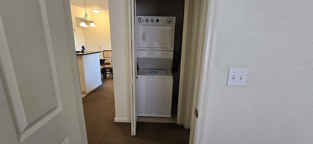 hallway featuring stacked washer / dryer, dark colored carpet, and a notable chandelier