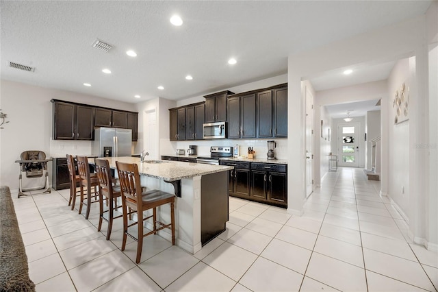 kitchen featuring sink, appliances with stainless steel finishes, a kitchen island with sink, a kitchen breakfast bar, and light stone countertops