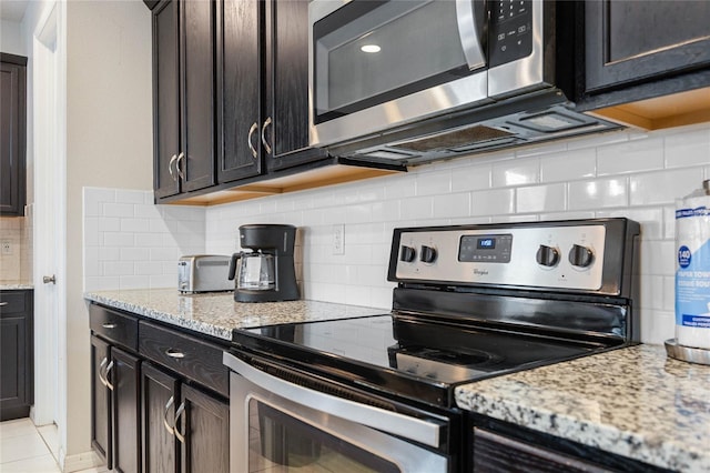 kitchen with stainless steel appliances, light stone countertops, dark brown cabinetry, and decorative backsplash