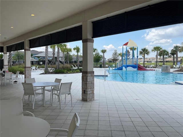 community pool with playground community, a patio, a water play area, and fence