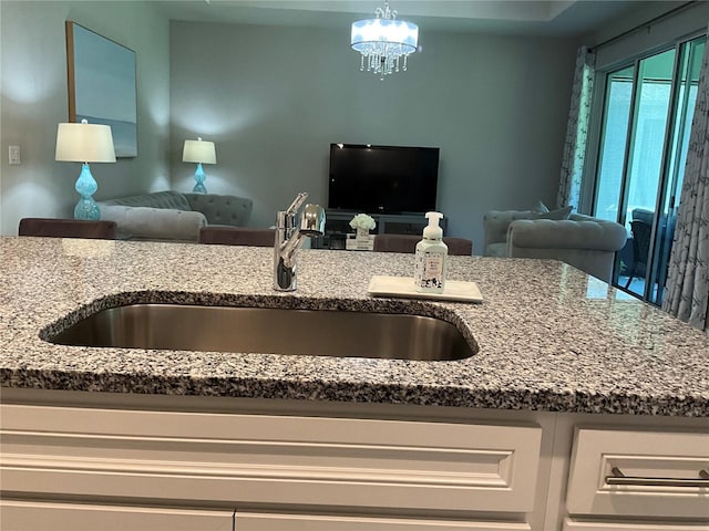 kitchen with light stone counters, a sink, open floor plan, hanging light fixtures, and an inviting chandelier