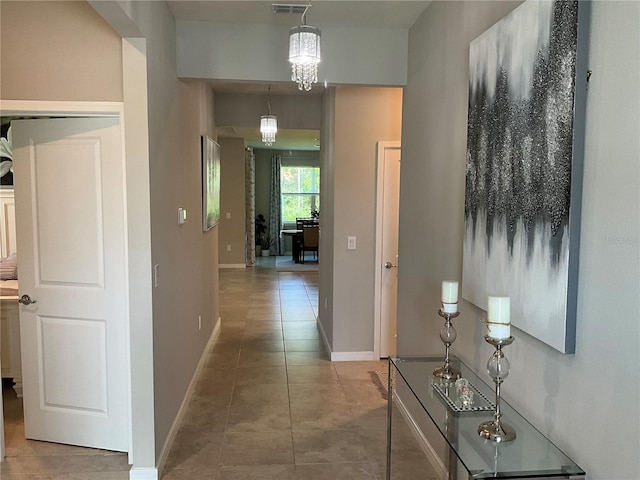hallway featuring visible vents, a notable chandelier, baseboards, and tile patterned floors