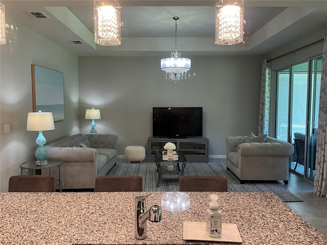 living area featuring an inviting chandelier, baseboards, visible vents, and a tray ceiling