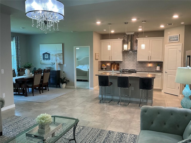 kitchen featuring wall chimney exhaust hood, open floor plan, decorative light fixtures, a kitchen island with sink, and white cabinetry