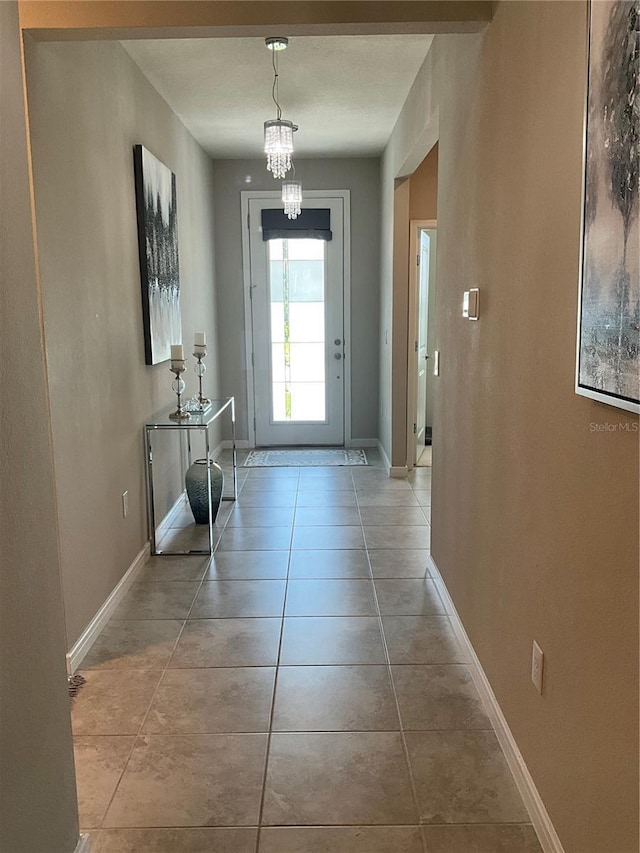 entryway with baseboards, an inviting chandelier, and light tile patterned floors