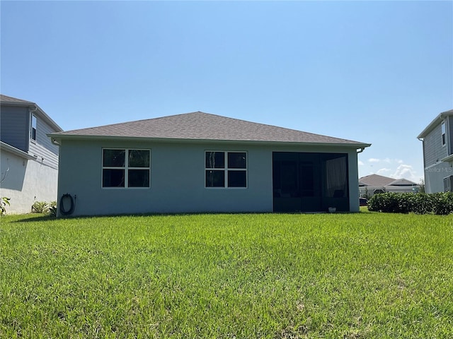 back of house with roof with shingles, a lawn, and stucco siding