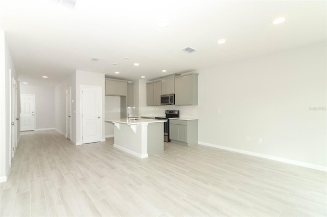 kitchen featuring gray cabinets, appliances with stainless steel finishes, sink, a kitchen island with sink, and light hardwood / wood-style floors