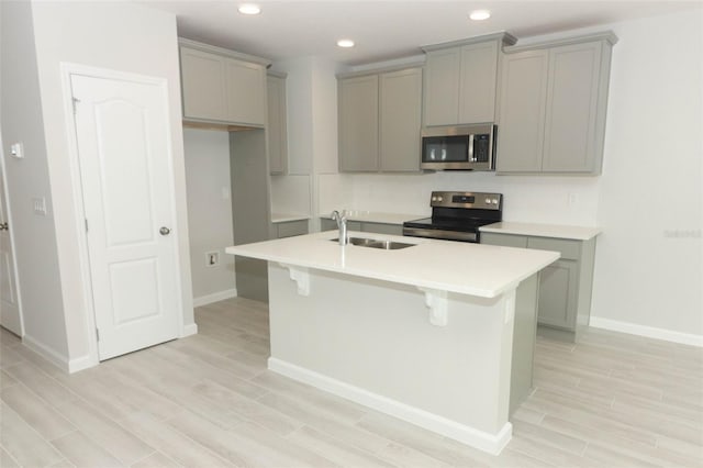 kitchen featuring stainless steel appliances, sink, a center island with sink, and gray cabinetry