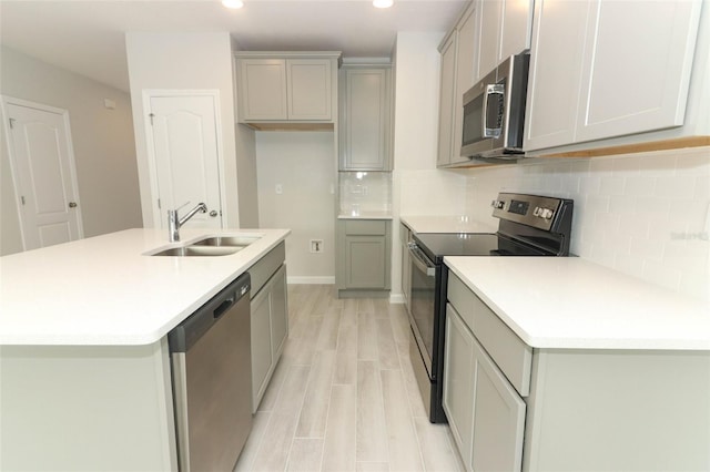 kitchen with sink, light hardwood / wood-style flooring, appliances with stainless steel finishes, tasteful backsplash, and a center island with sink