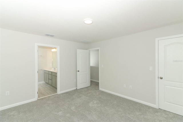 unfurnished bedroom featuring light carpet and ensuite bath