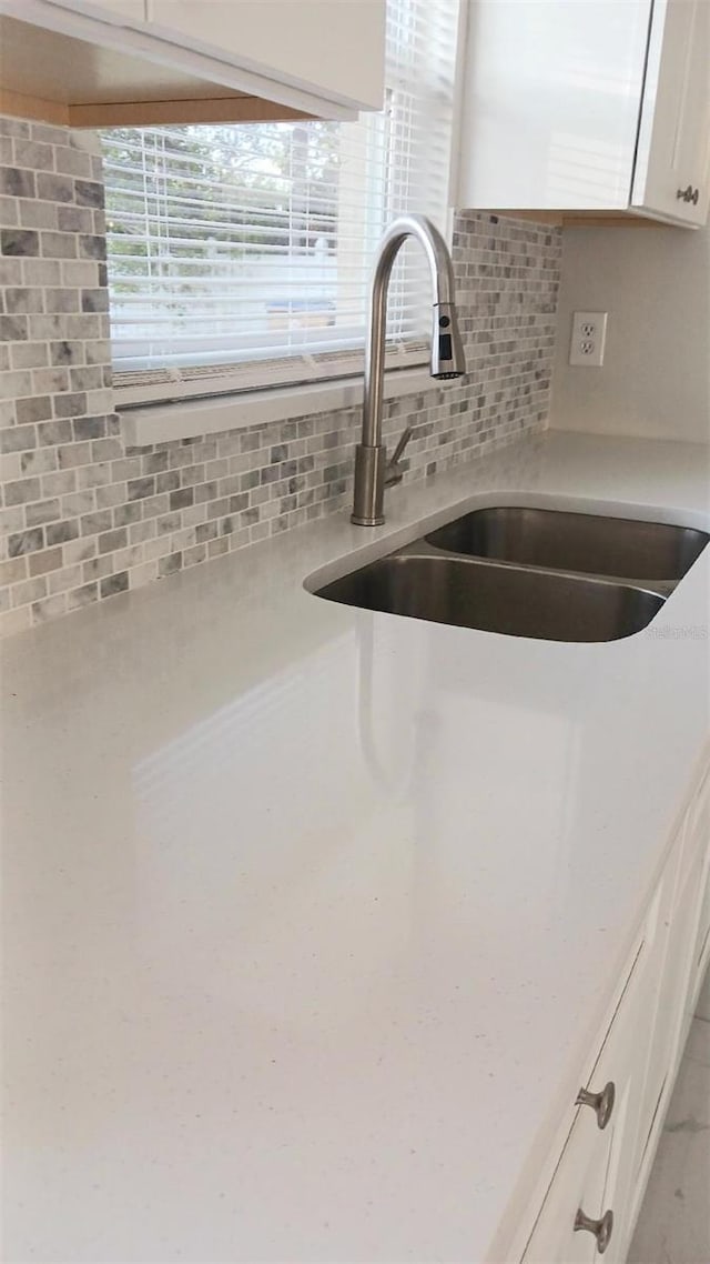 interior details with white cabinetry, sink, and decorative backsplash