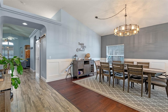 dining room with ceiling fan with notable chandelier, lofted ceiling, hardwood / wood-style floors, and a barn door