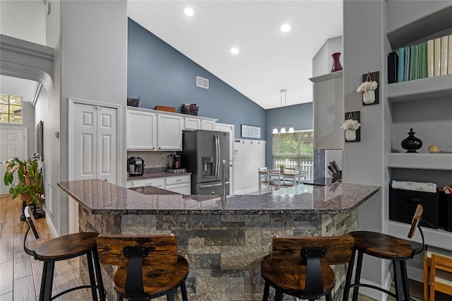 kitchen with a breakfast bar area, white cabinetry, stainless steel refrigerator with ice dispenser, and kitchen peninsula