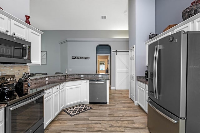 kitchen featuring stainless steel appliances, white cabinets, dark stone counters, a barn door, and sink