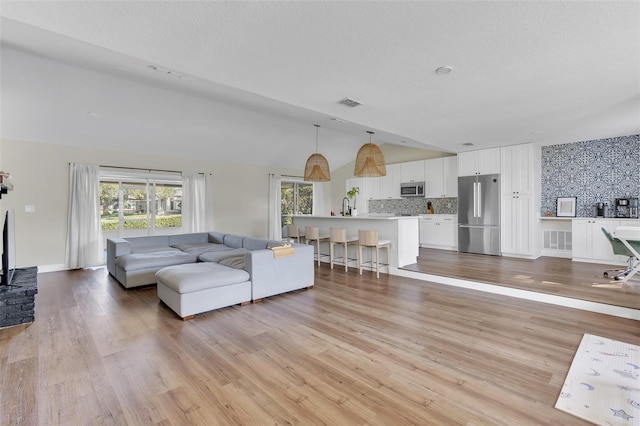 living room with lofted ceiling, sink, a textured ceiling, and light wood-type flooring