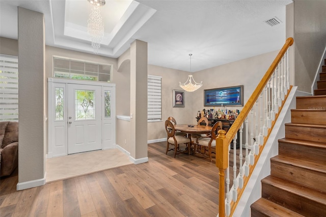 foyer entrance featuring a raised ceiling, wood-type flooring, and an inviting chandelier