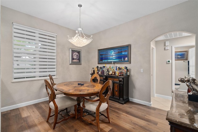 dining room with hardwood / wood-style floors, a chandelier, and bar area