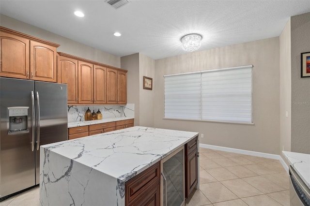 kitchen featuring appliances with stainless steel finishes, tasteful backsplash, wine cooler, a center island, and light stone counters