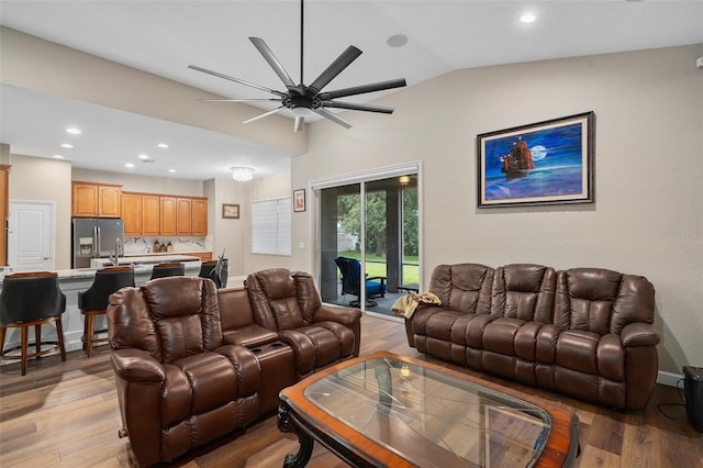 living room with ceiling fan, vaulted ceiling, and light wood-type flooring