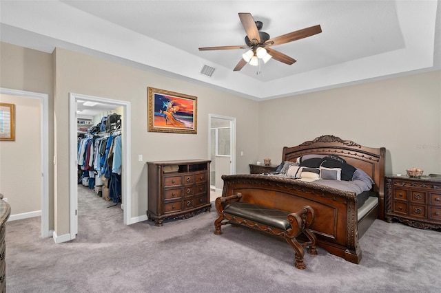 carpeted bedroom featuring a closet, a walk in closet, a raised ceiling, and ceiling fan