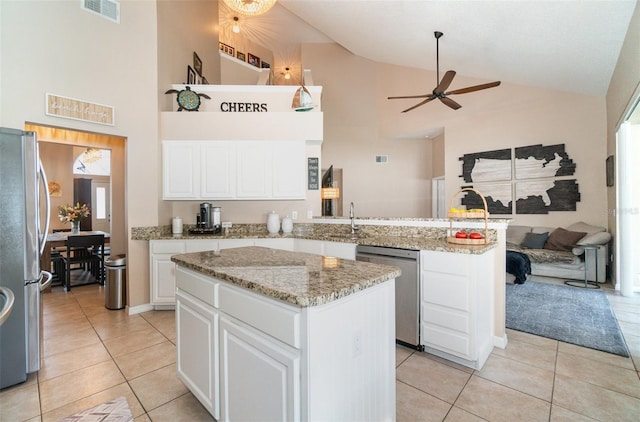 kitchen with appliances with stainless steel finishes, light tile patterned floors, a kitchen island, white cabinets, and light stone countertops