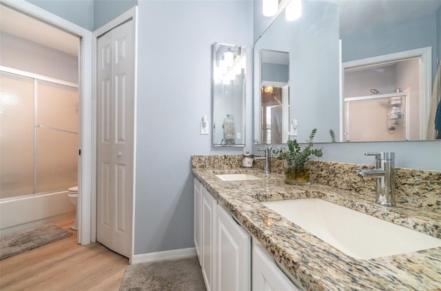 full bathroom with hardwood / wood-style flooring, enclosed tub / shower combo, vanity, and toilet