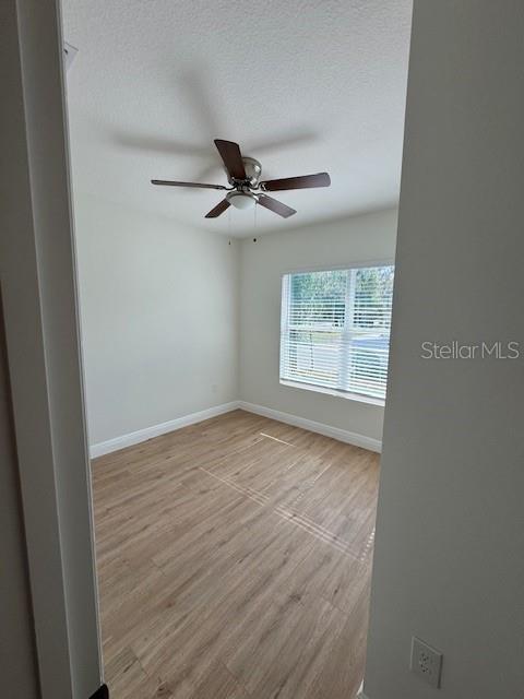 spare room with ceiling fan, a textured ceiling, and light wood-type flooring