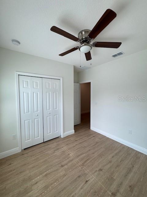 unfurnished bedroom featuring ceiling fan, light hardwood / wood-style floors, and a closet