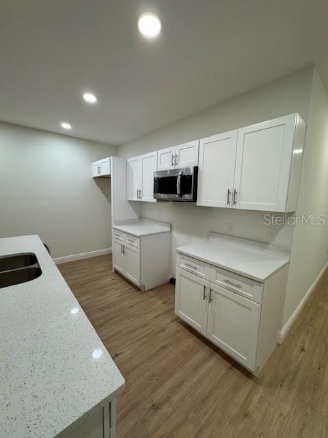 kitchen with white cabinetry, sink, hardwood / wood-style flooring, and light stone countertops