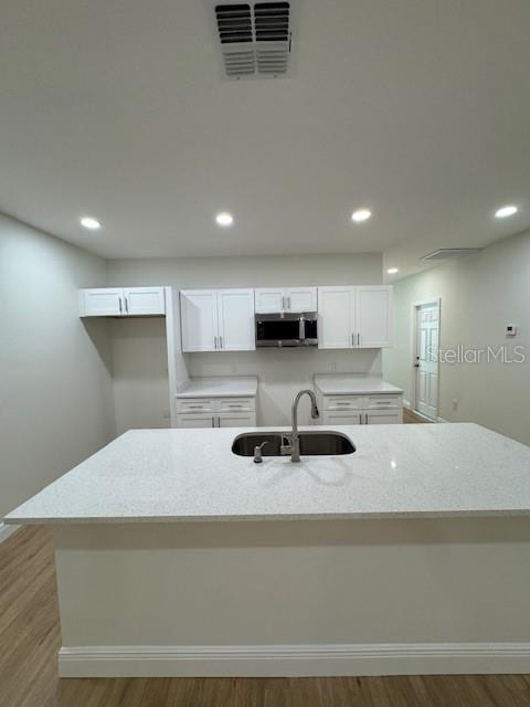 kitchen with white cabinetry, light stone countertops, sink, and light hardwood / wood-style floors