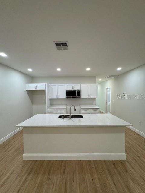 kitchen featuring white cabinetry, sink, an island with sink, and hardwood / wood-style flooring