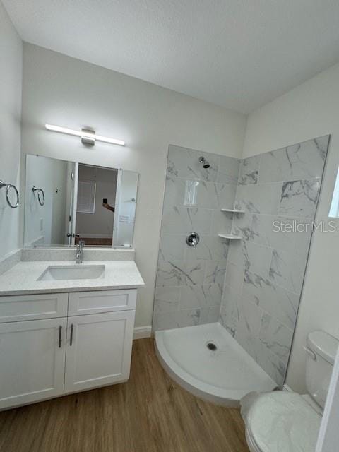 bathroom featuring vanity, toilet, wood-type flooring, and a tile shower